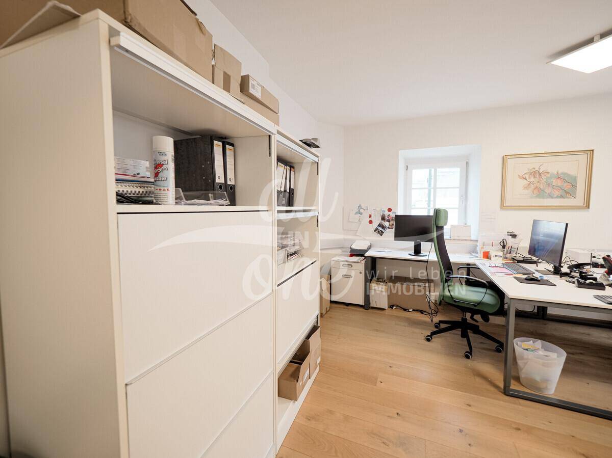Helles Büro mit Schreibtischen, Bürostühlen und einem großen Regal für Akten und Materialien.