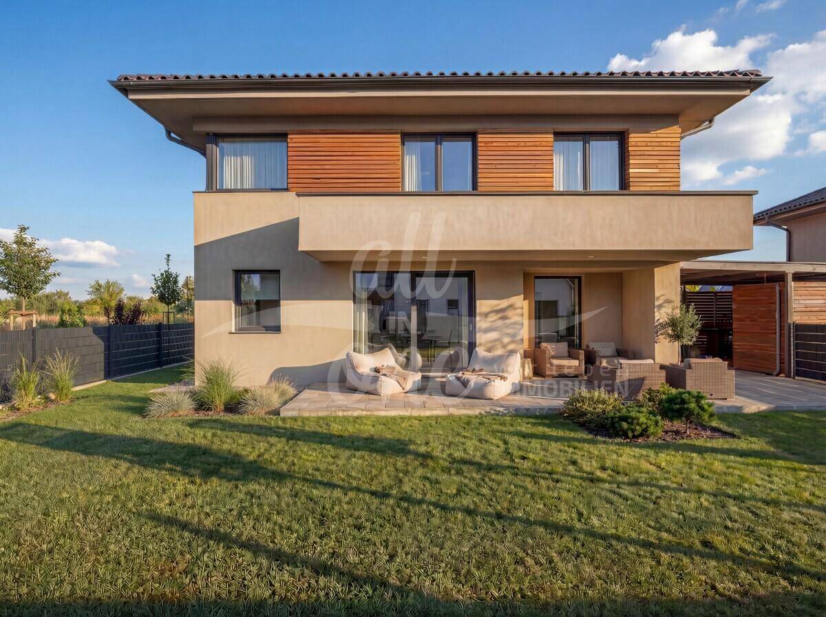Rückseite der modernen Villa mit kleiner Terrasse, Lounge-Möbeln und weitläufigem Rasenbereich.