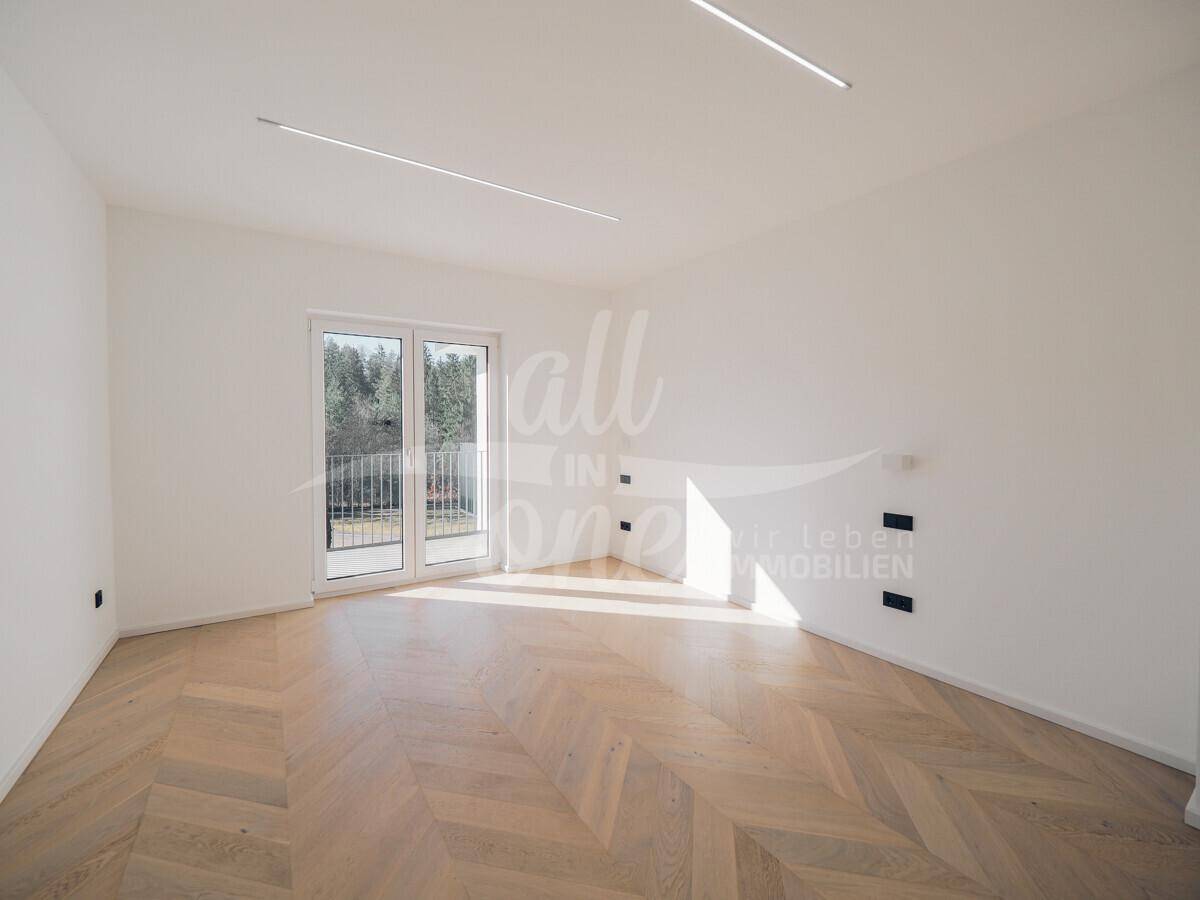 Heller Raum mit Fischgrätparkett, modernen Deckenleuchten und Zugang zu einem französischen Balkon.