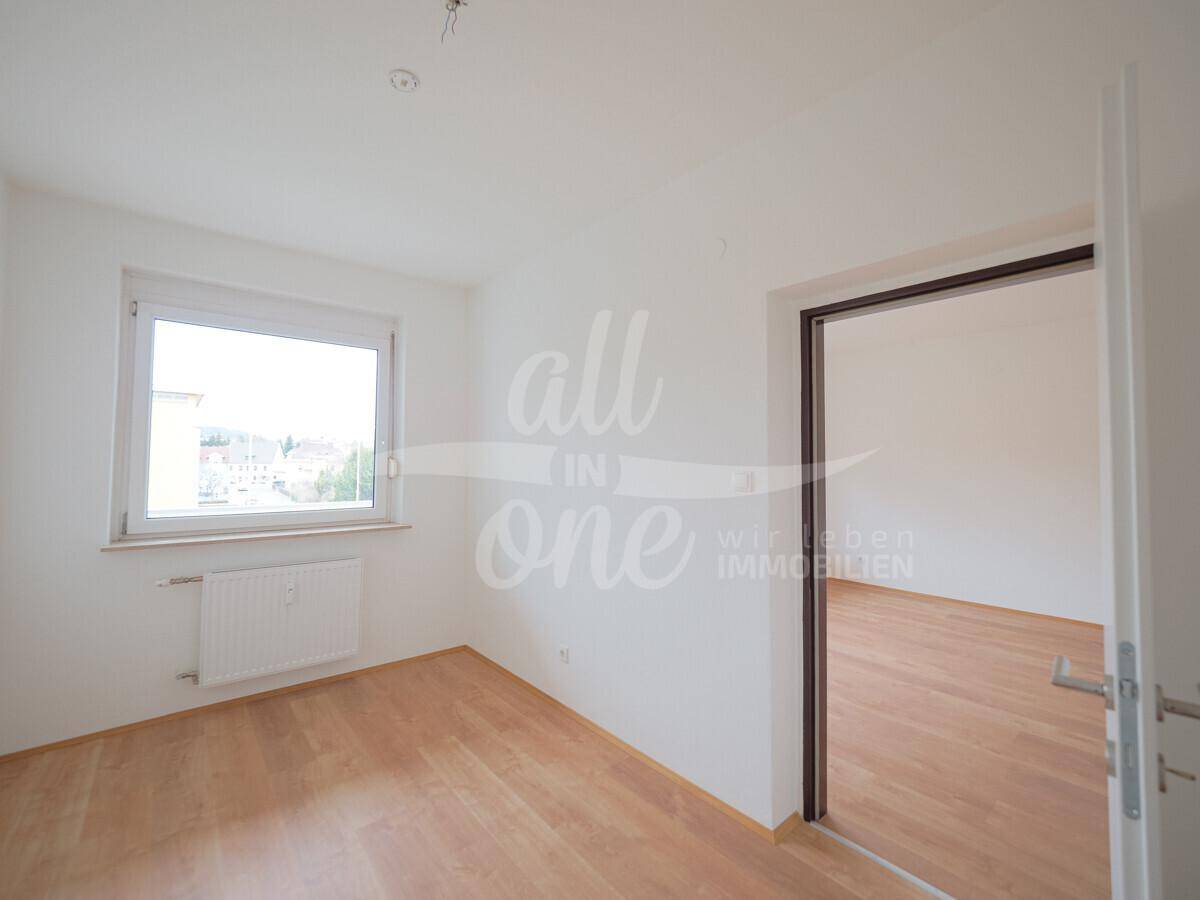 Leeres Schlafzimmer mit Laminatboden, weiß gestrichenen Wänden und einem Fenster.