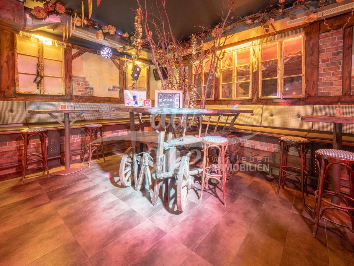 Gemütlicher Sitzbereich mit Holztischen, Bänken und einem dekorativen Wagenrad-Tisch in rustikalem Ambiente.