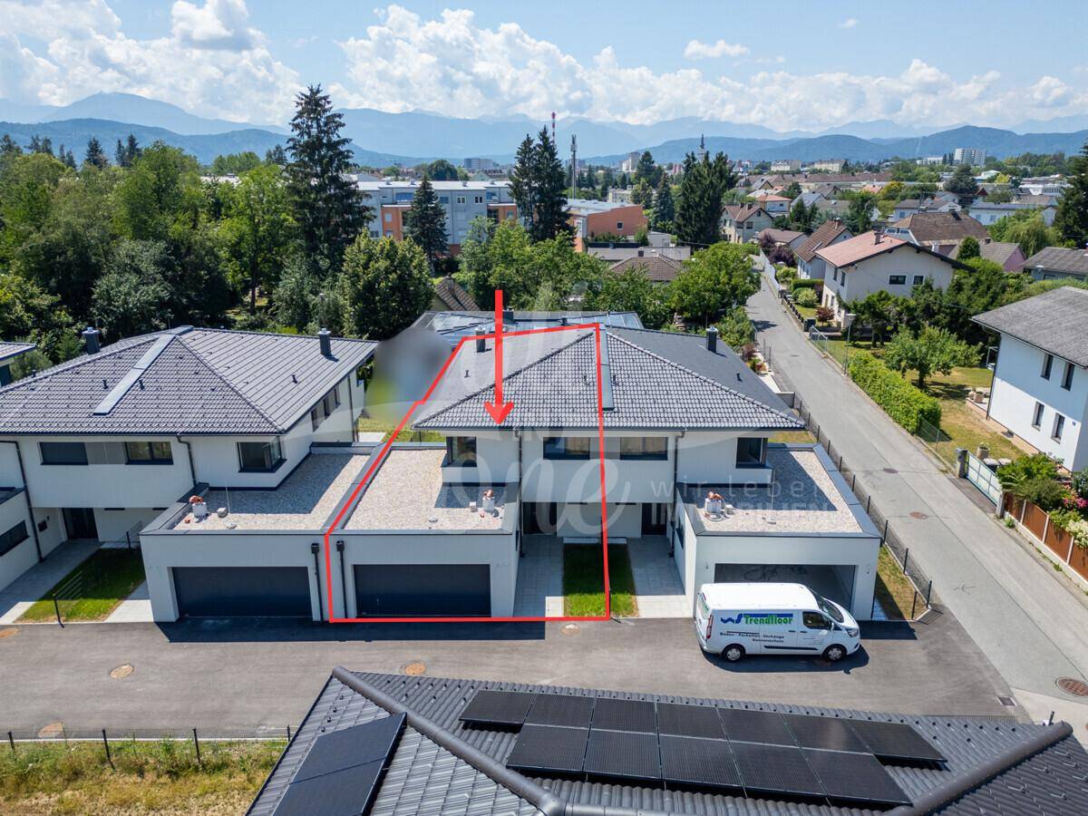 Luftaufnahme eines modernen Wohnkomplexes mit Reihenhäusern und Garagen in grüner Umgebung.
