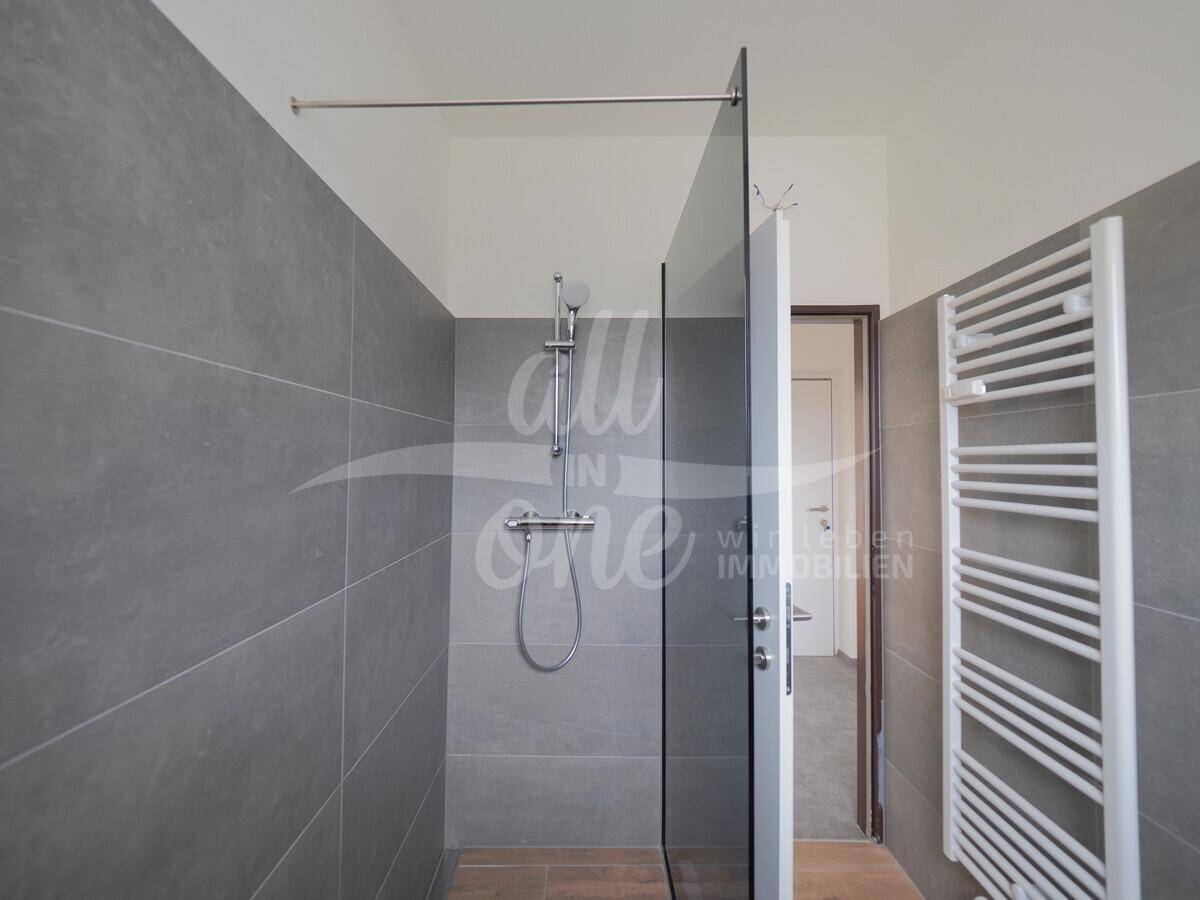 Modernes Badezimmer mit großer begehbarer Dusche und grauen Fliesen.