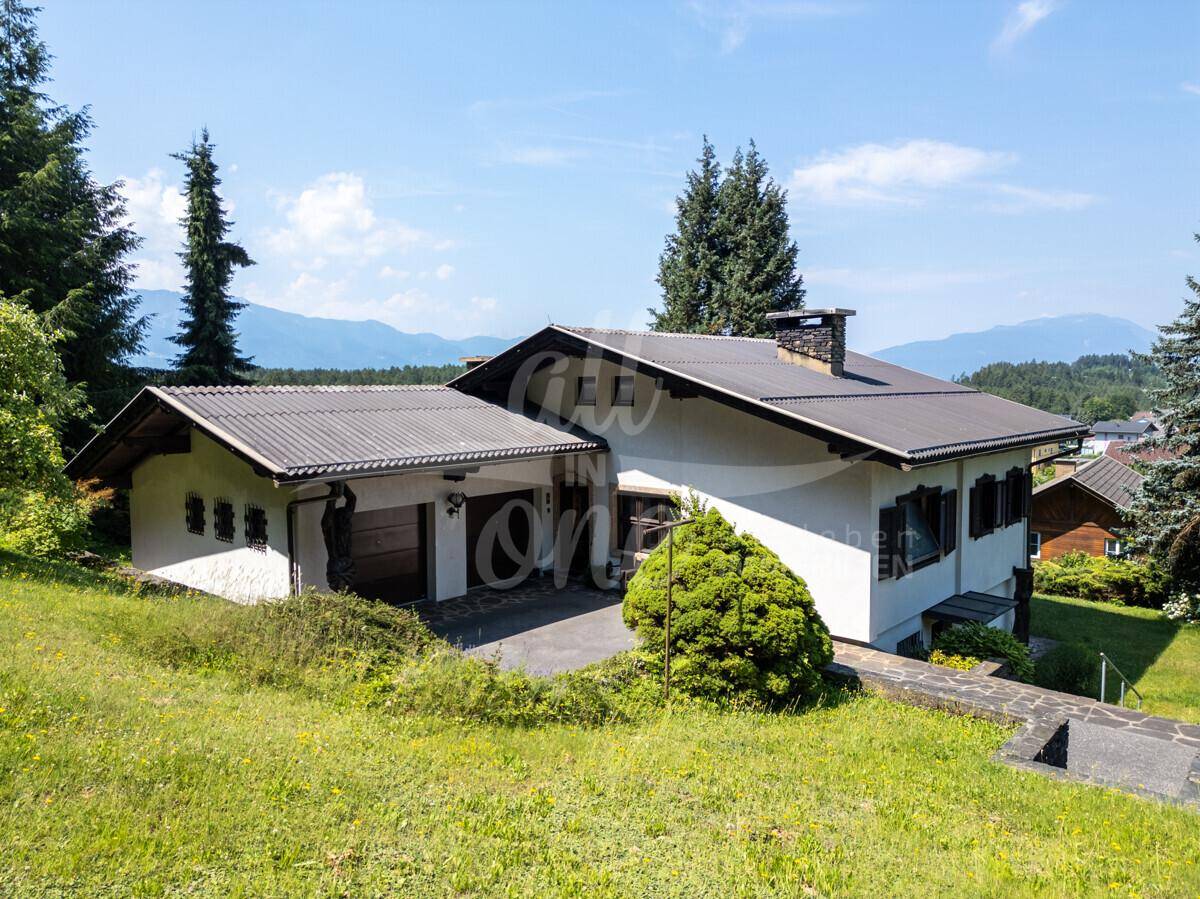 Seitenansicht des Hauses mit integrierter Garage und gepflegtem Gartenbereich unter blauem Himmel.