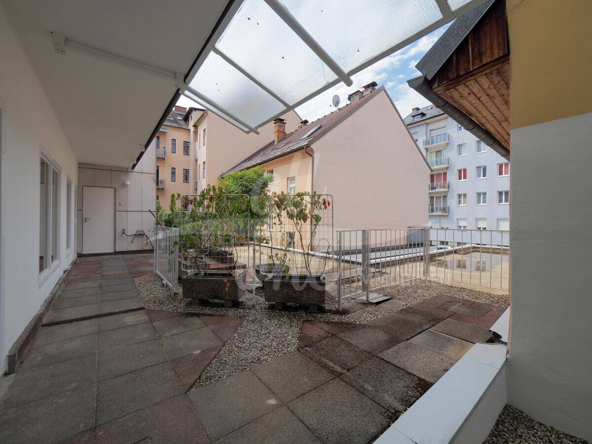 Große, gepflasterte Terrasse mit Pflanzenkübeln und Blick auf umliegende Gebäude.