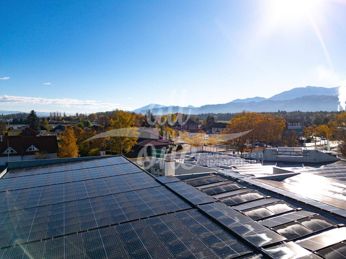 Nahaufnahme von Solarmodulen auf einem Gebäudedach mit Bergen und blauem Himmel im Hintergrund.