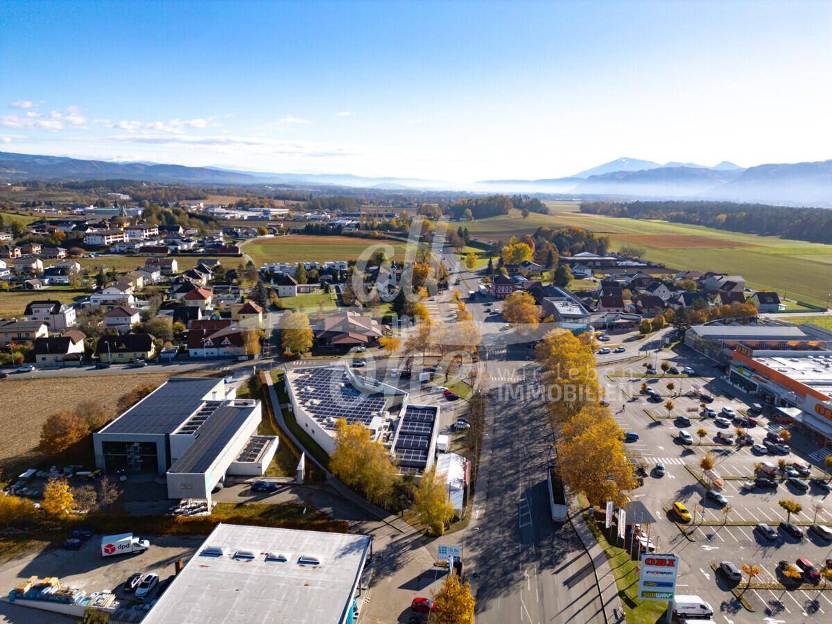 Luftaufnahme eines Gewerbeparks mit großem Parkplatz, umgeben von Natur und Wohngebieten.