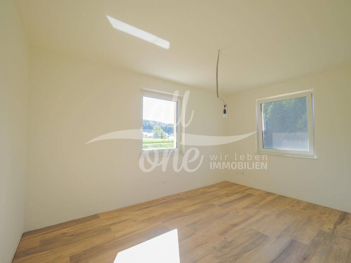 Helles Zimmer mit Holzboden und Fenster, das viel Tageslicht und einen weiten Blick bietet.