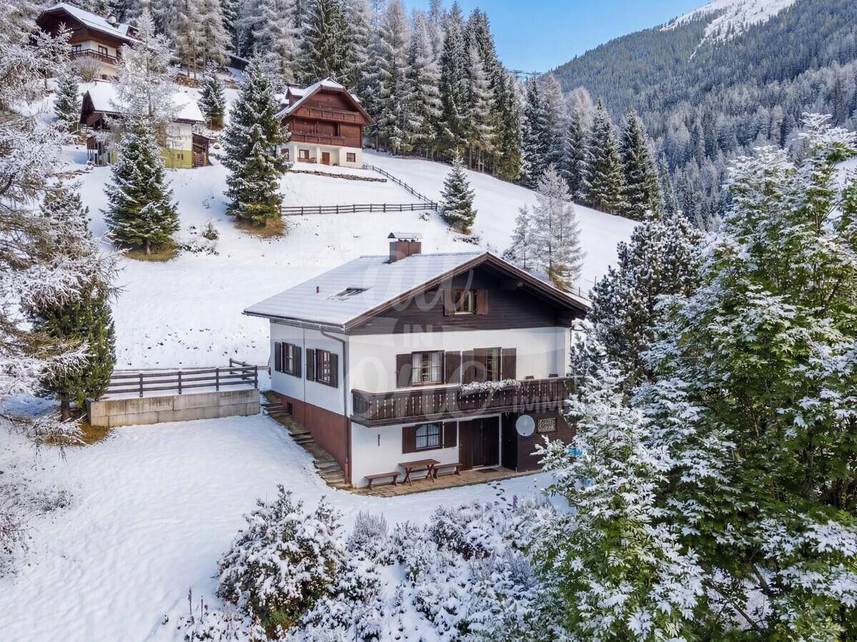 Traditionelles Haus in verschneiter Berglandschaft mit Balkon und umliegenden Wäldern.
