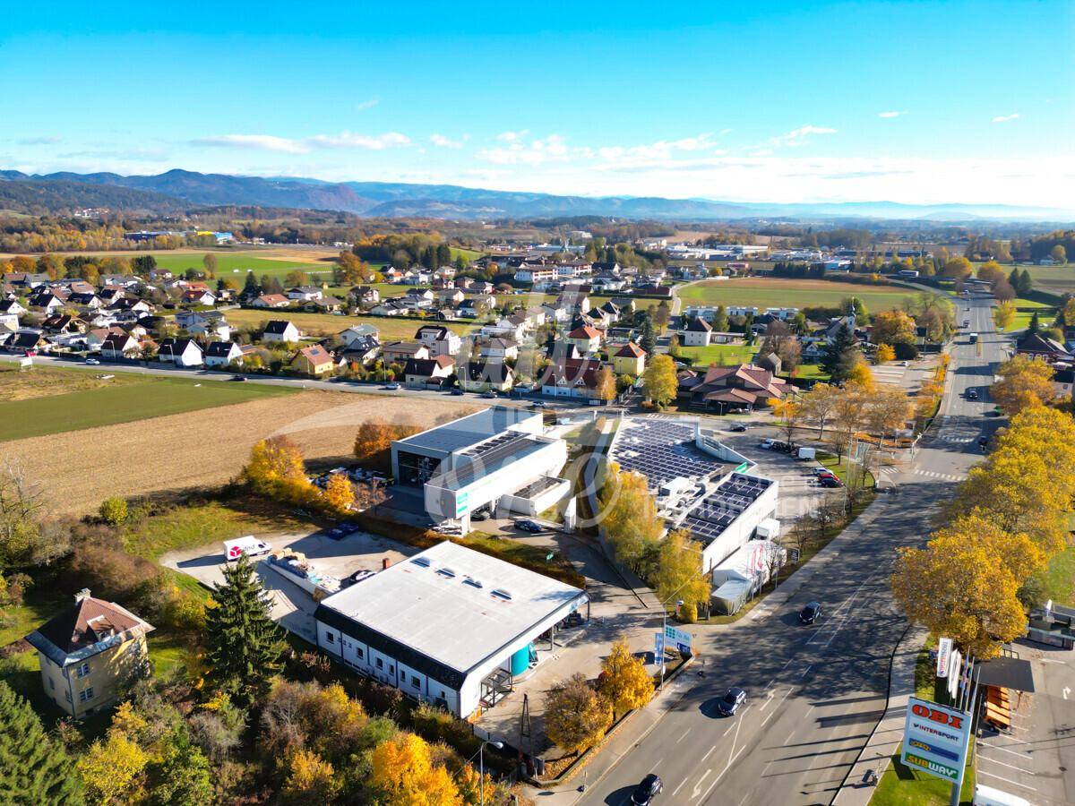 Panoramablick auf ein Gewerbegebiet, eingebettet in eine ländliche Umgebung mit Wohngebäuden und Bergen.