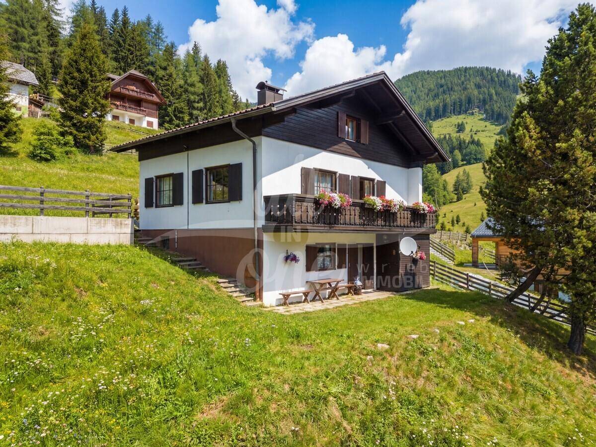 Charmantes Haus mit Balkon und Blumenkästen, umgeben von grünen Hügeln und Wäldern.
