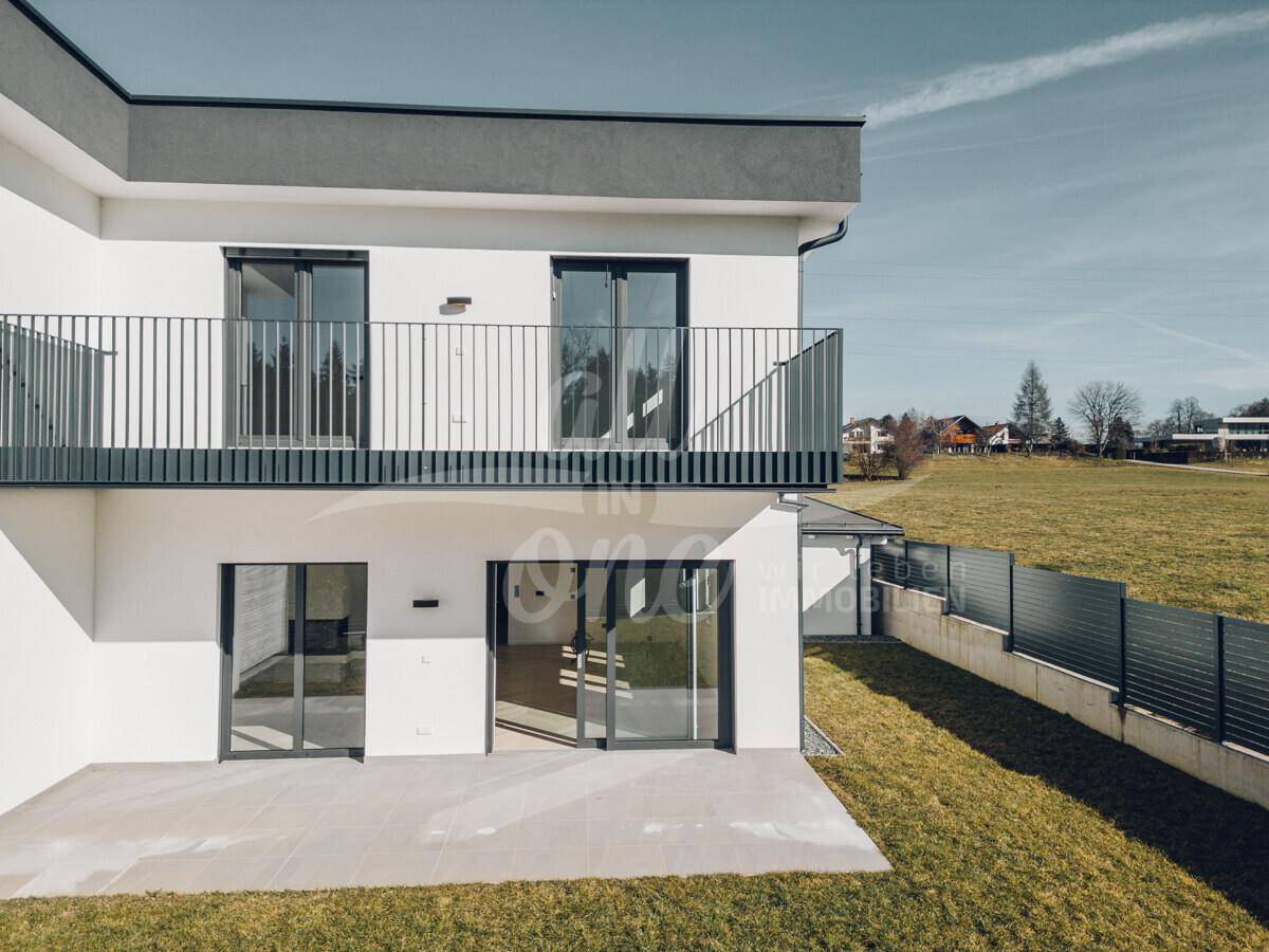 Rückansicht des modernen Hauses mit Balkon, Terrasse und weitem Blick ins Grüne.