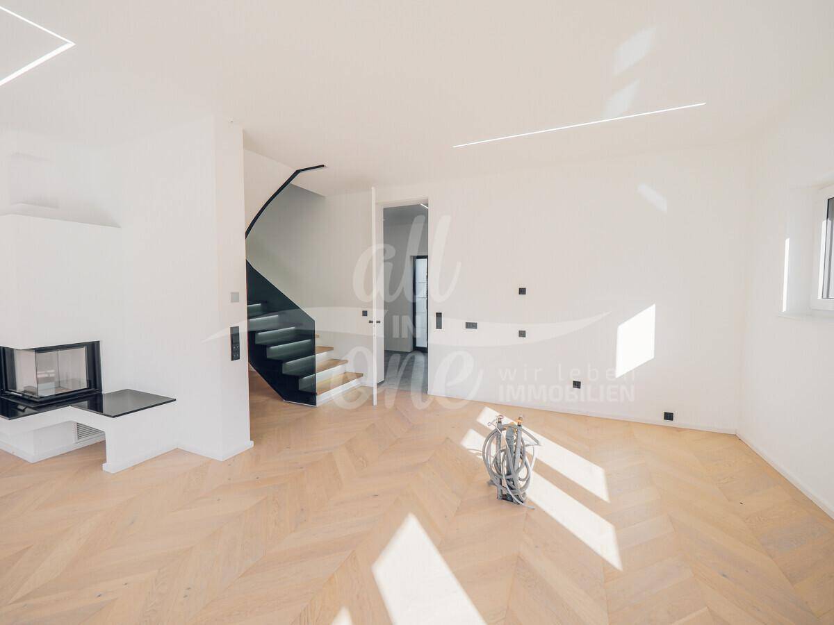 Heller Wohnbereich mit eleganter Treppe, Fischgrätparkett und Zugang zum Flur.