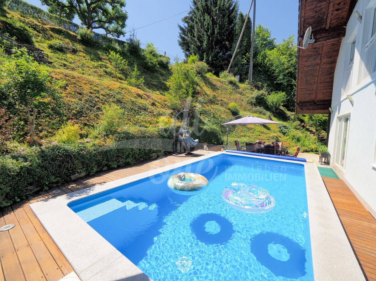 Großer Swimmingpool mit Holzdeck und Blick auf den grünen Hang.