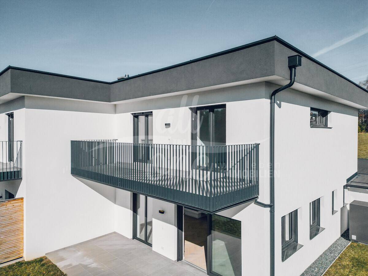 Moderne Architektur mit weißer Fassade, dunklem Flachdach und eleganten Balkonen.