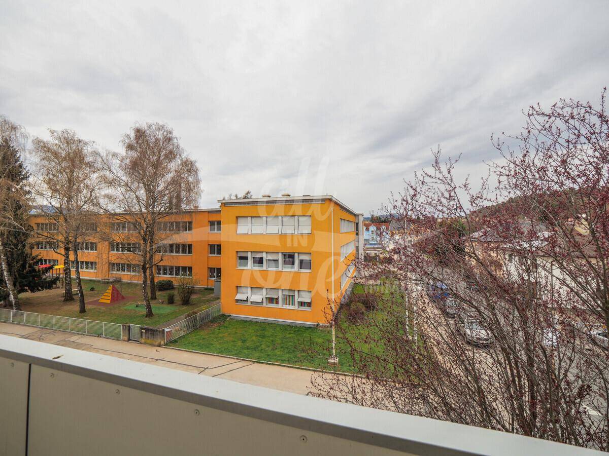 Balkon mit Ausblick auf ein gegenüberliegendes Schulgebäude und Grünflächen.