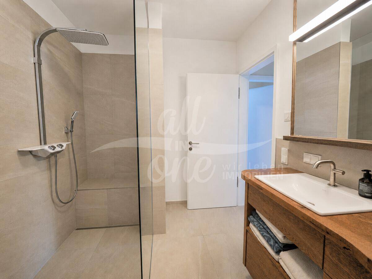 Modernes Badezimmer mit begehbarer Dusche, beigefarbenen Fliesen und Holzwaschtisch.
