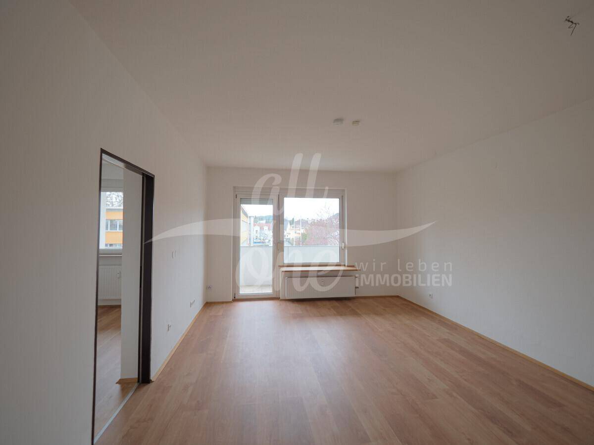 Helles Wohnzimmer mit Laminatboden und Zugang zum Außenbereich.