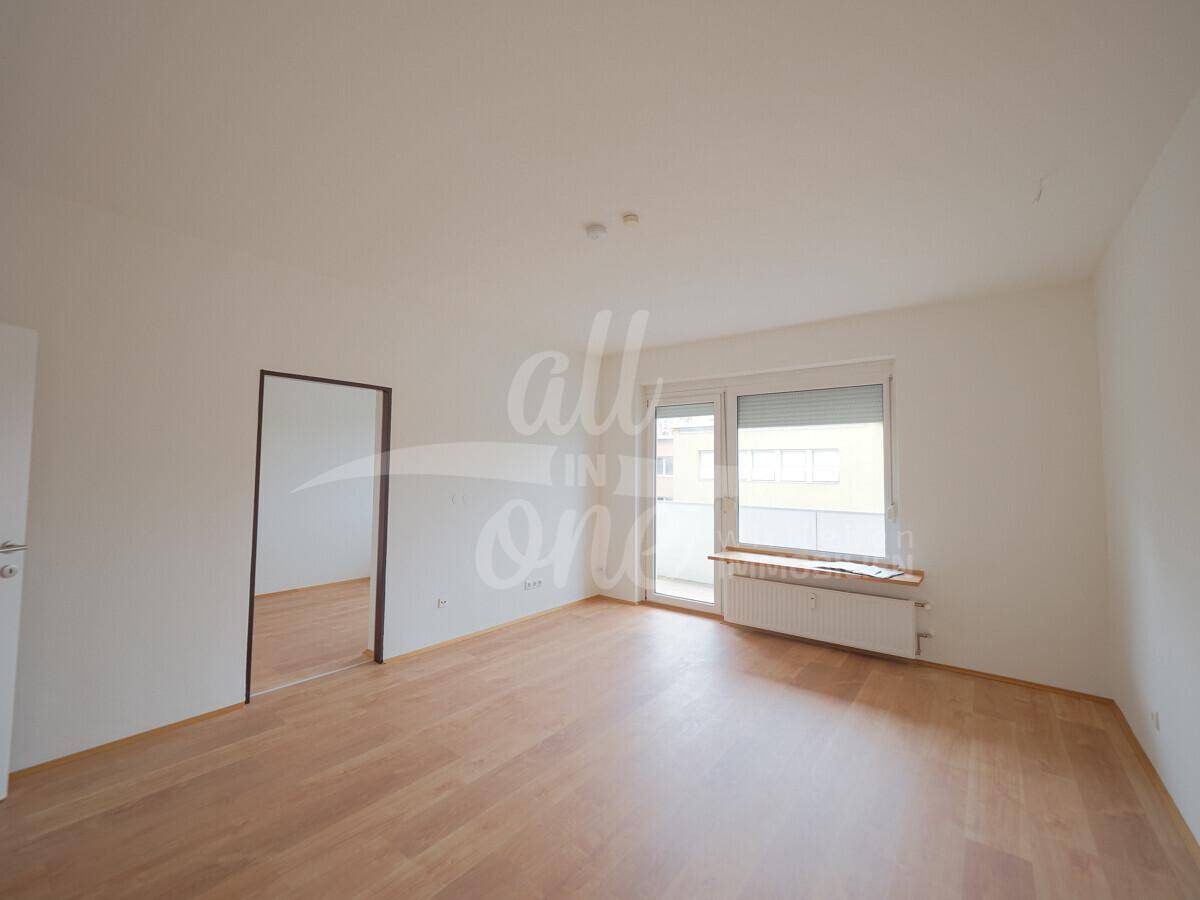 Geräumiges Wohnzimmer mit hellem Laminatboden und Fenster mit Rollladen.
