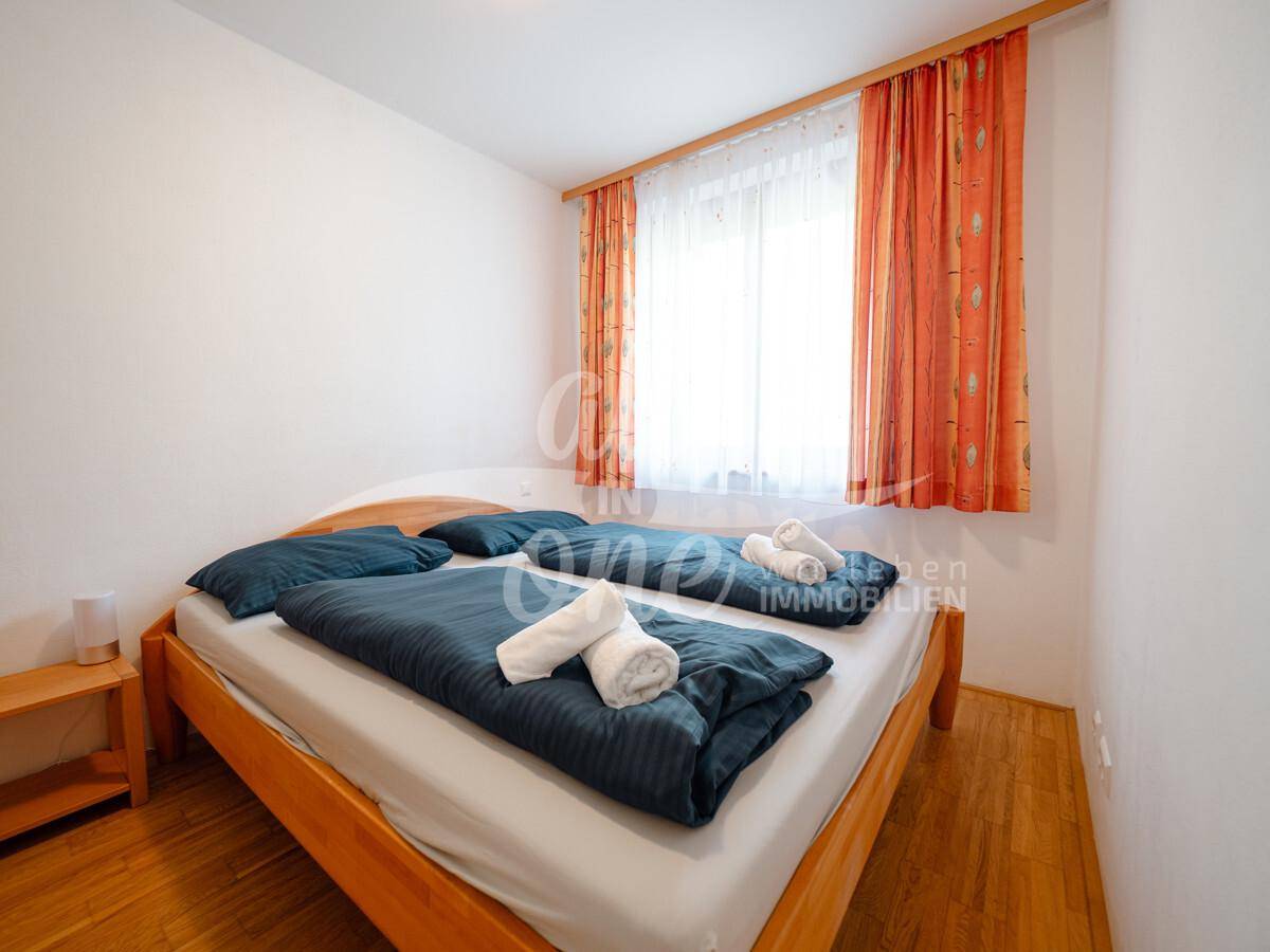 Schlafzimmer mit Doppelbett, Holzboden und einem Fenster mit farbigen Vorhängen.
