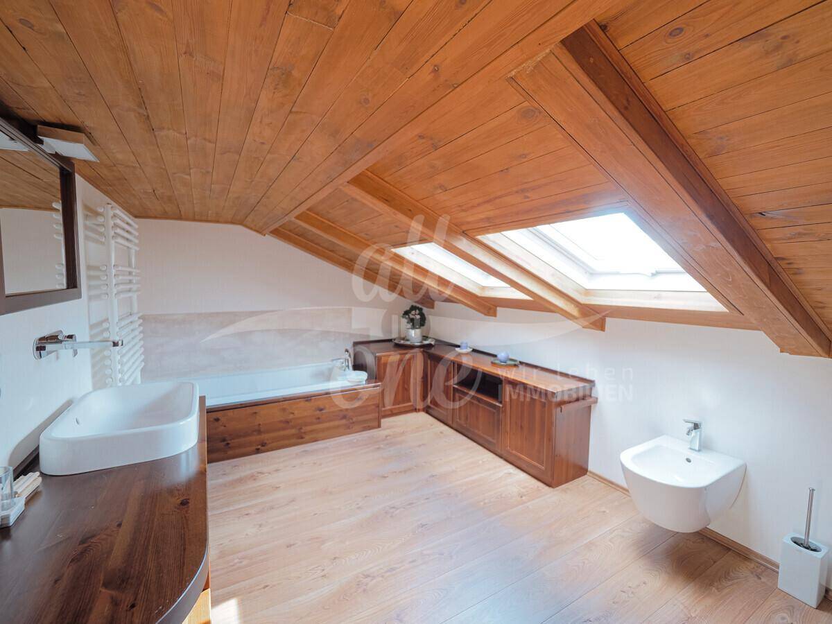 Modernes Badezimmer im Dachgeschoss mit Badewanne, Waschbecken und Dachfenster.