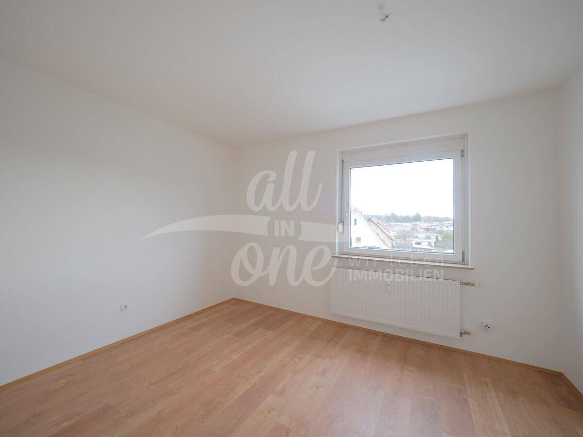 Helles Schlafzimmer mit Laminatboden und Blick auf die umliegenden Häuser.