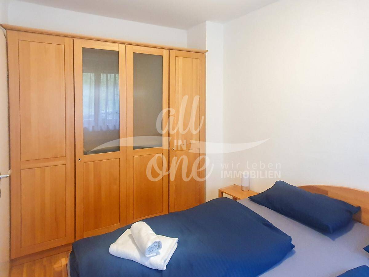 Schlafzimmer mit Doppelbett und großem Holzschrank mit Spiegeltüren, auf Holzboden.