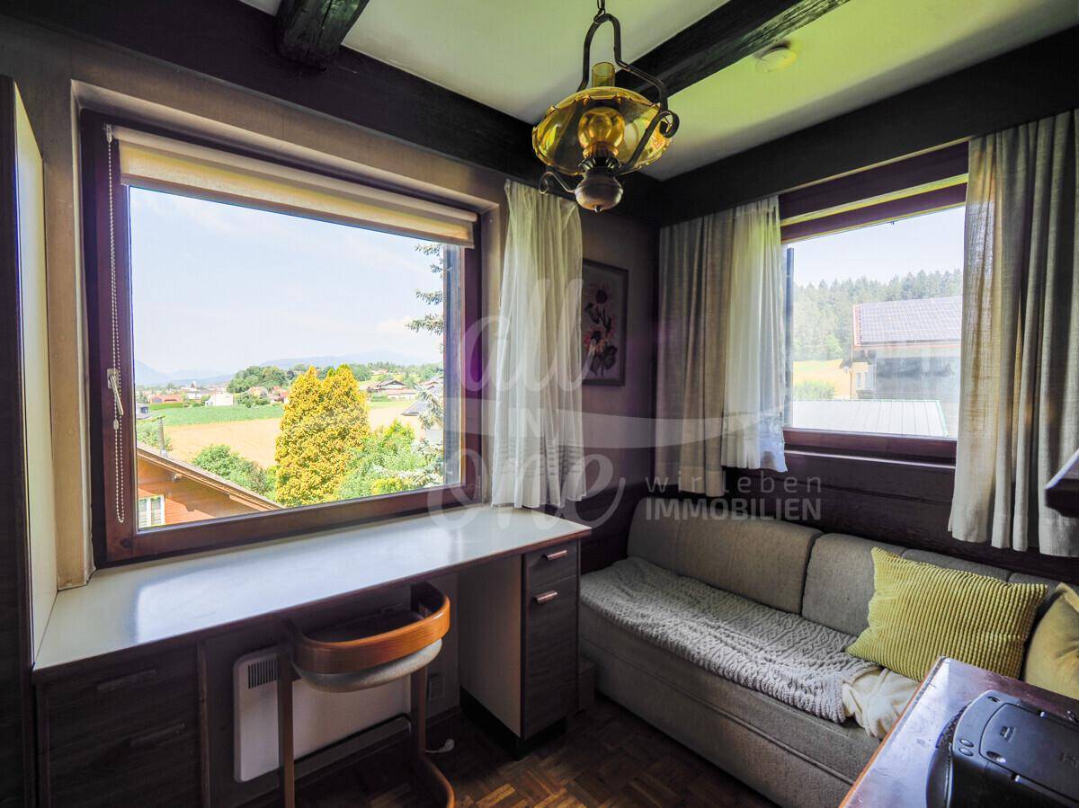 Kleines Zimmer mit Schreibtisch, Sofa und großem Fenster mit weitem Blick in die Landschaft.