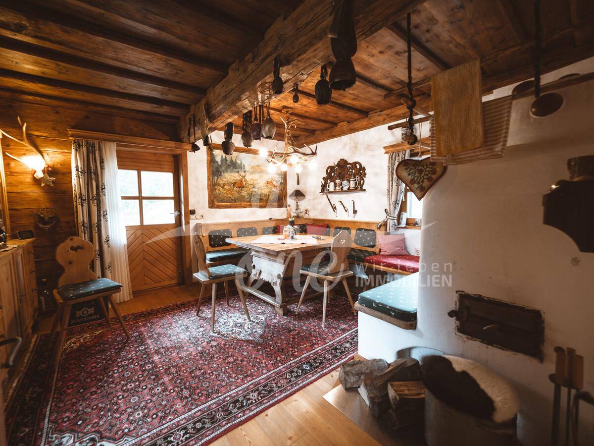 Gemütlicher Essbereich im Landhausstil mit Holzbalkendecke, Kachelofen und traditionellem Teppich.