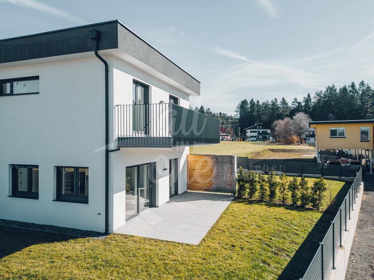 Ansicht der modernen Hausfassade mit Balkon, Terrasse und umzäuntem Gartenbereich.