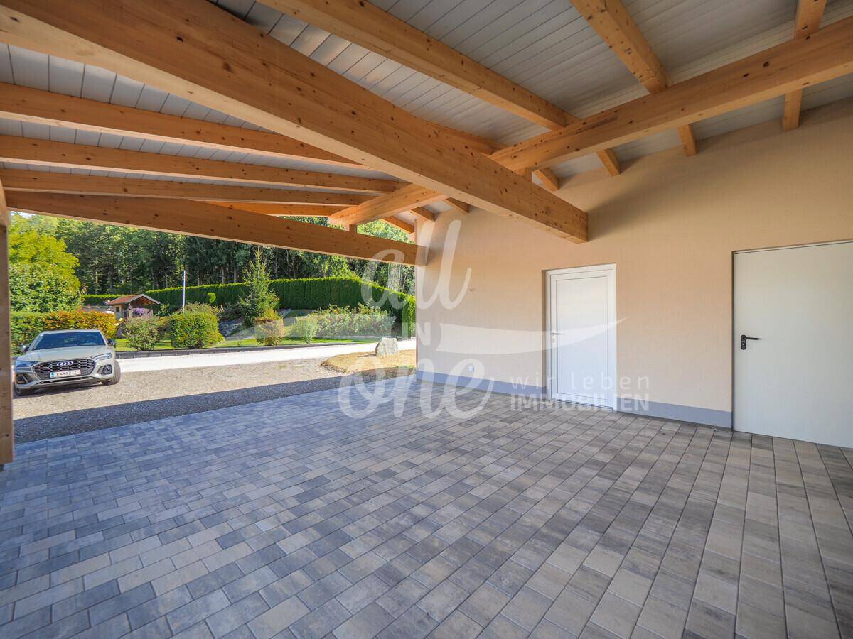 Geräumiger Carport mit Holzbalkenkonstruktion und gepflastertem Boden, bietet Schutz für Fahrzeuge.