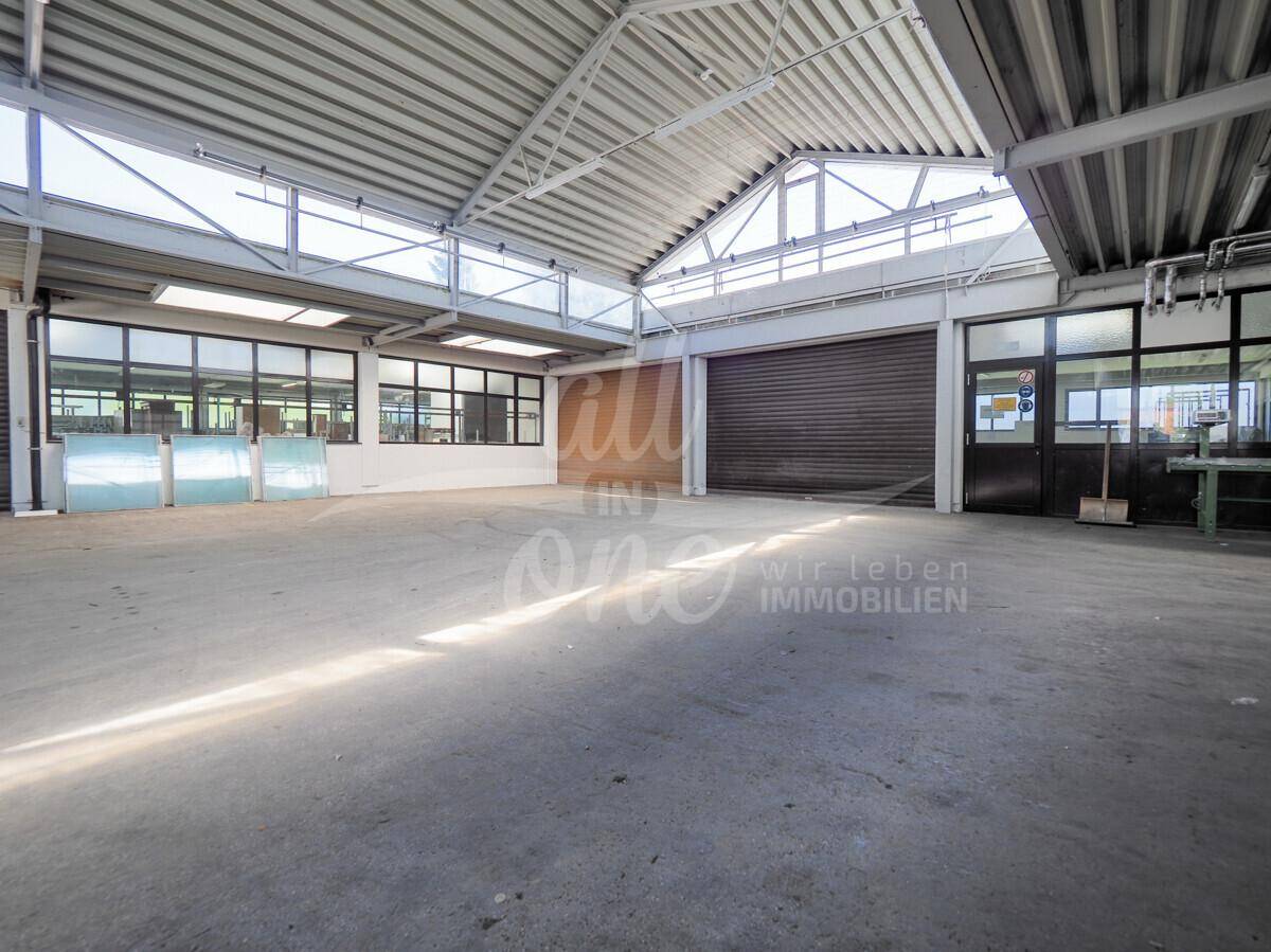 Helle Lagerhalle mit hohen Decken, großen Fenstern und Rolltoren, ideal für gewerbliche Zwecke.
