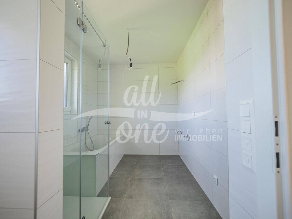 Geräumiges Badezimmer mit weißen Fliesen, vorbereitet für die Installation von Waschtisch und Armaturen.