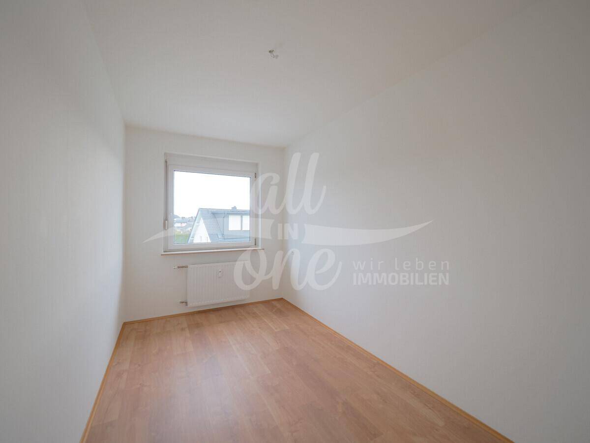 Leeres Schlafzimmer mit Laminatboden und einem Fenster, das viel Tageslicht hereinlässt.