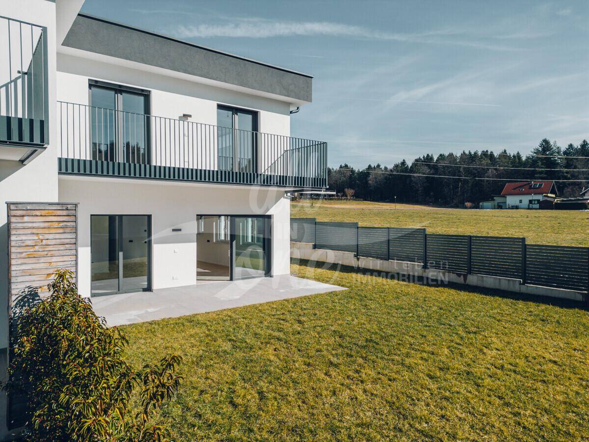 Moderne Hausfassade mit großzügiger Rasenfläche und einer Terrasse im Erdgeschoss.