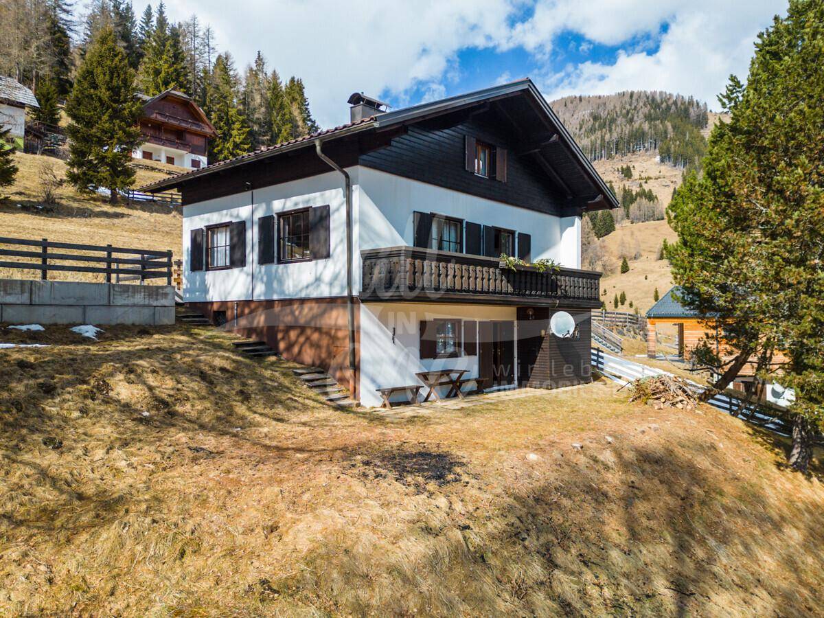 Traditionelles Haus in alpiner Umgebung mit Balkon, grüner Wiese und Bergblick.