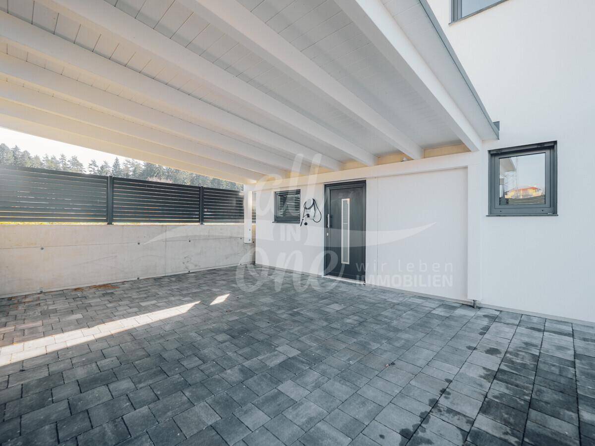 Überdachter Carport-Bereich mit gepflastertem Boden und direktem Zugang zum Hauseingang.
