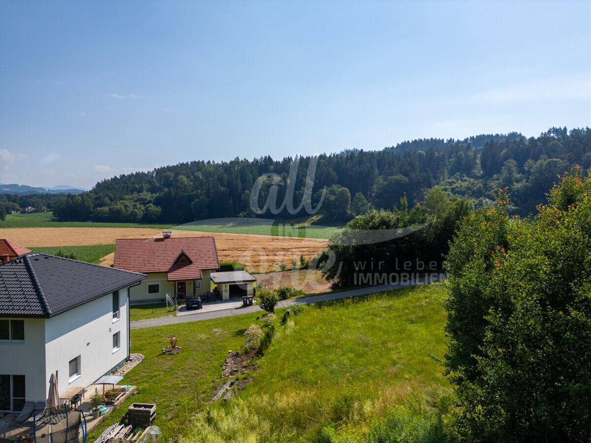 Panoramablick auf die ländliche Umgebung mit Wohnhäusern, Feldern und bewaldeten Hügeln.