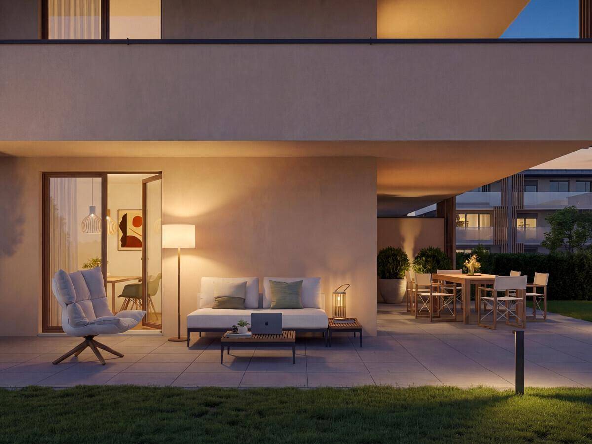 Beleuchtete Terrasse mit modernen Sitzgelegenheiten und Rasenfläche am Abend.