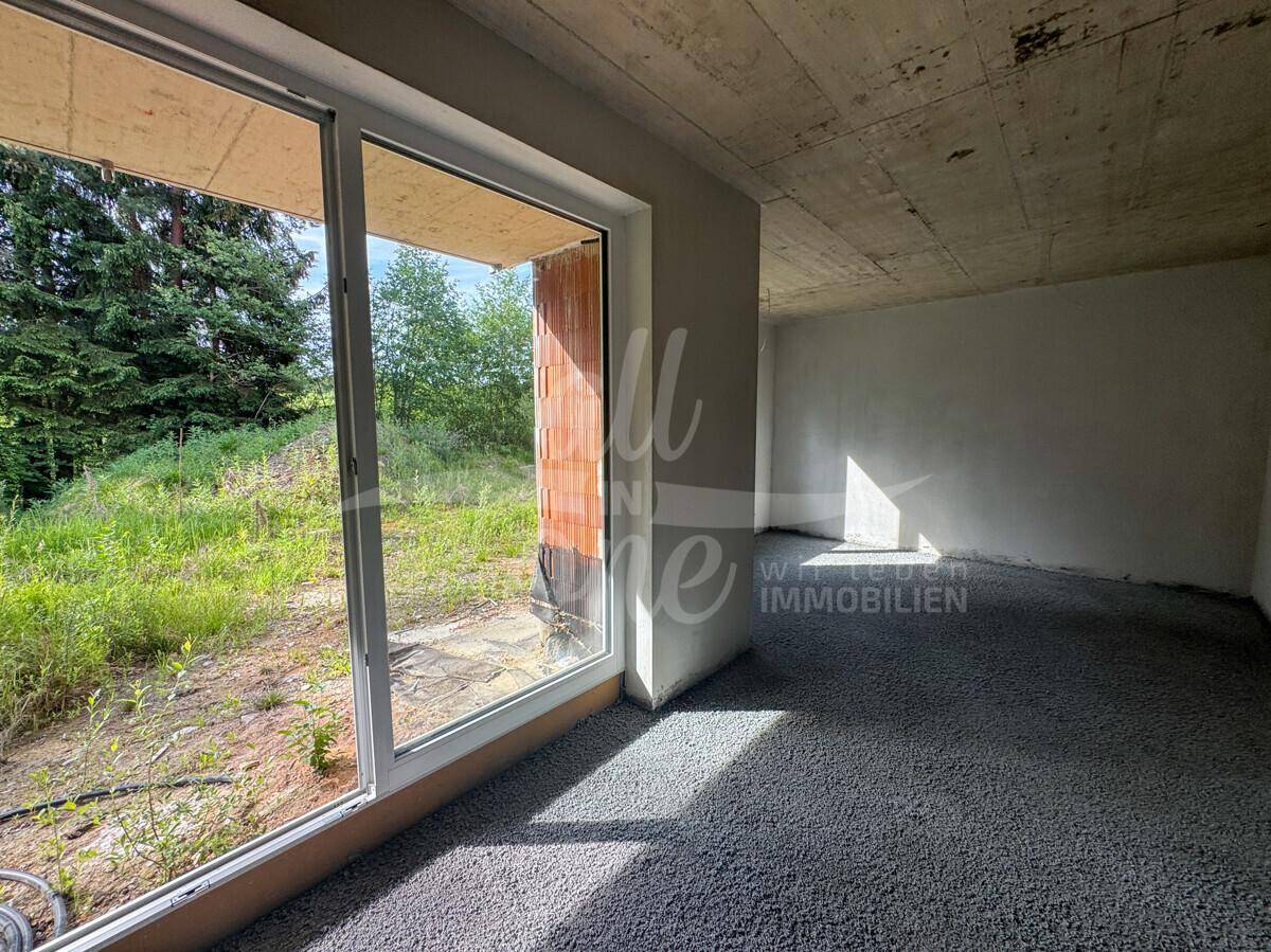 Helles Rohbau-Zimmer mit großem Fenster und direktem Zugang zur Außenterrasse.