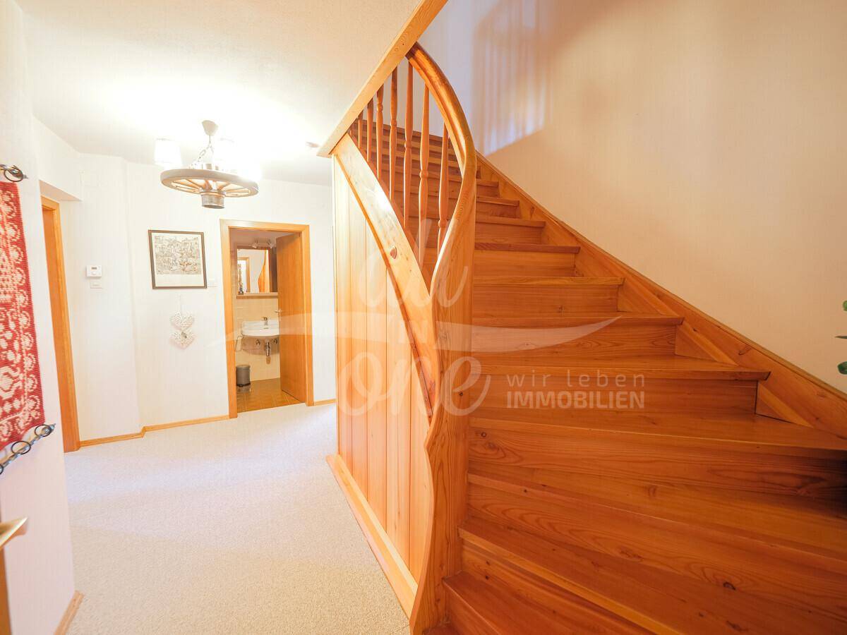 Heller Flur mit Holztreppe und Zugang zu einem Badezimmer.