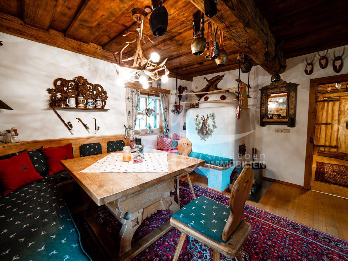 Traditioneller Essbereich mit Holztisch, Eckbank und einem dekorativen Kachelofen, unter Holzbalken.
