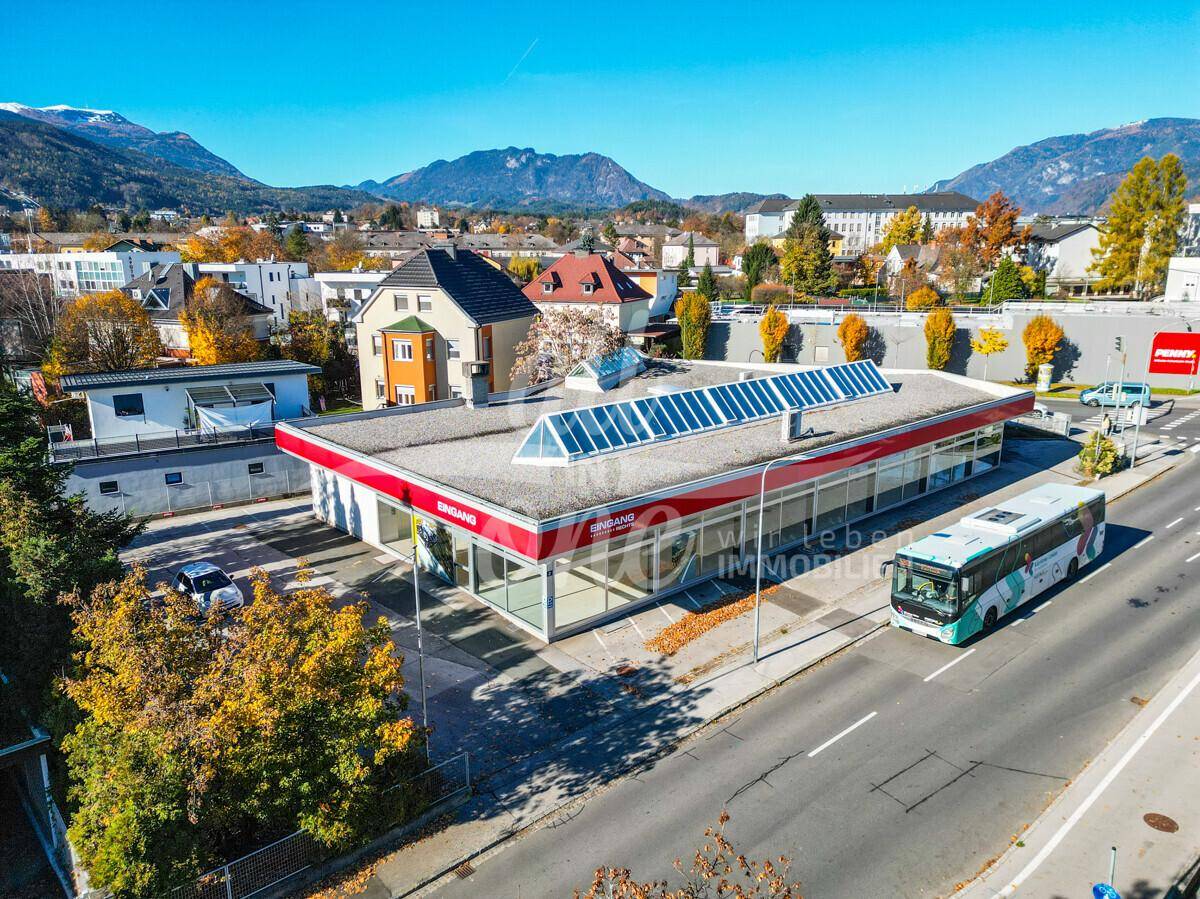 Luftaufnahme des Geschäftsgebäudes mit Solaranlage auf dem Dach, umgeben von städtischer Infrastruktur und Bergen im Hintergrund.