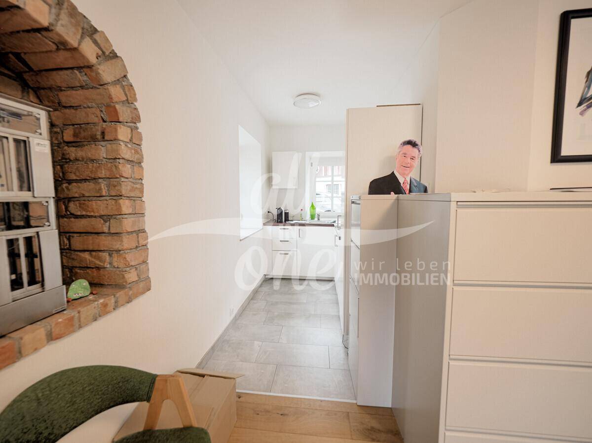 Heller Flur mit Holzboden, der zu einer kleinen, funktionalen Küchenzeile führt.