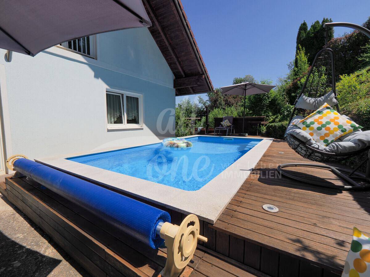 Außenpool mit Holzdeck, Sonnenschirm und bequemen Sitzgelegenheiten.