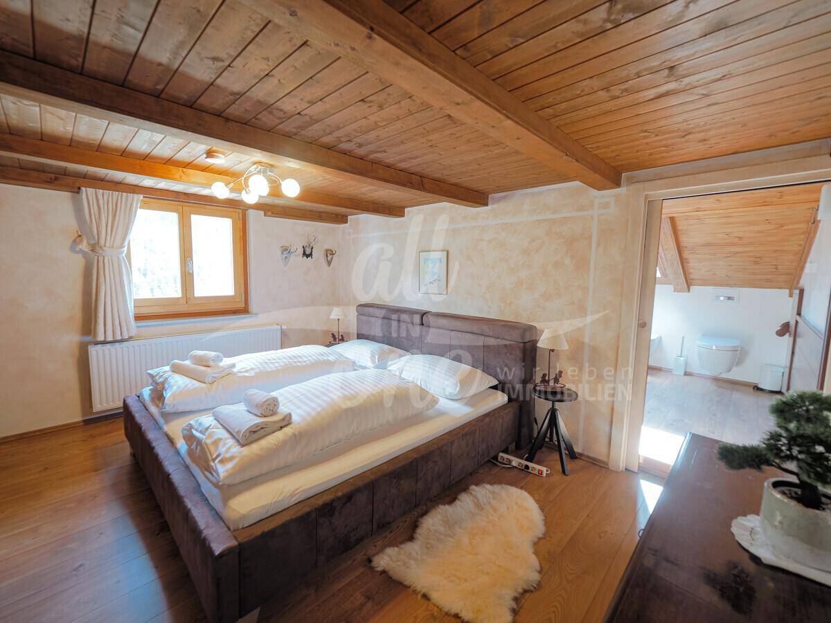 Helles Schlafzimmer im Dachgeschoss mit Holzbalken und Zugang zum Badezimmer.