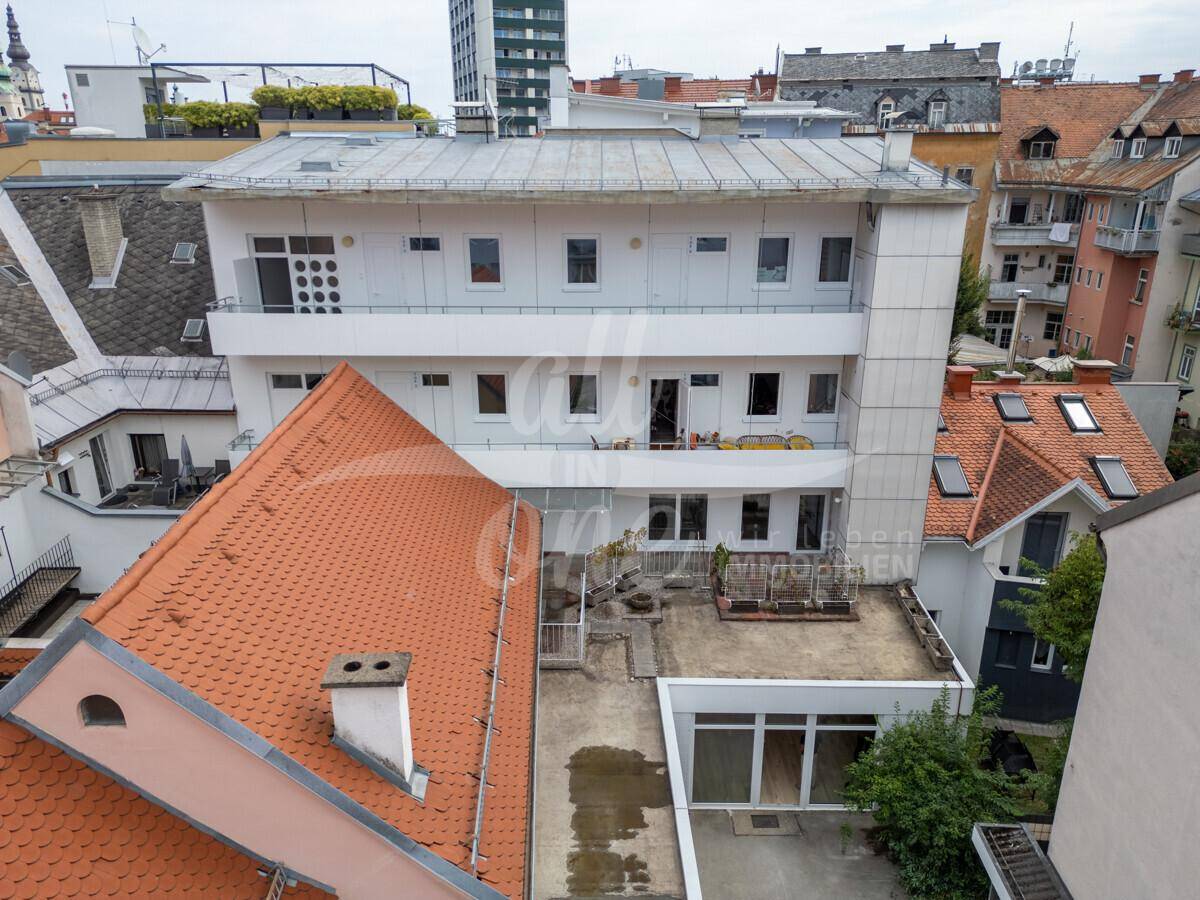 Luftaufnahme eines Mehrfamilienhauses mit Flachdach und umliegenden Gebäuden in städtischer Umgebung.