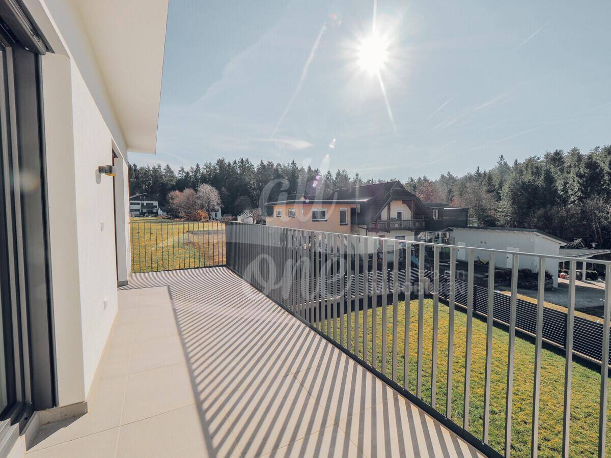 Sonniger Balkon mit Fliesenboden und Blick auf die grüne Landschaft und benachbarte Häuser.