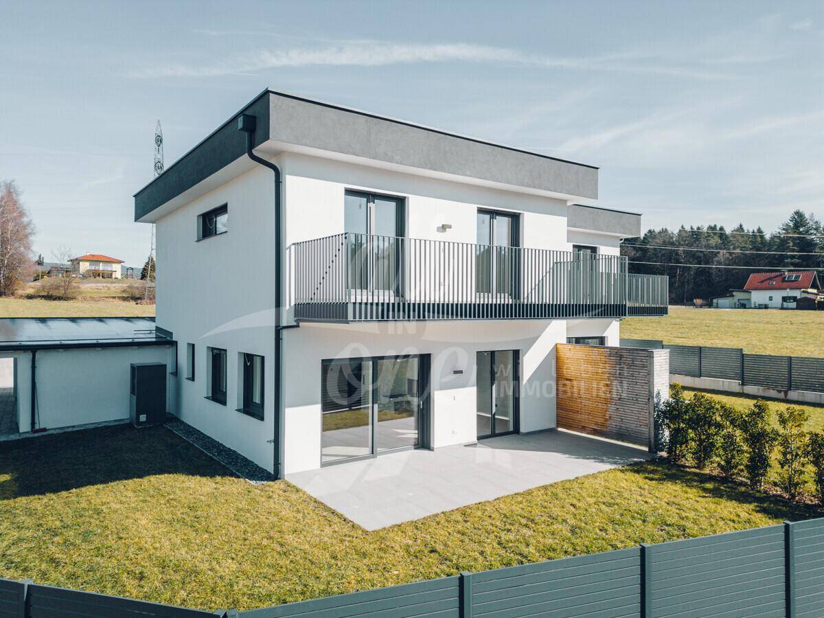 Moderne Neubaufassade mit Balkon, Terrasse und gepflegtem Rasenbereich.