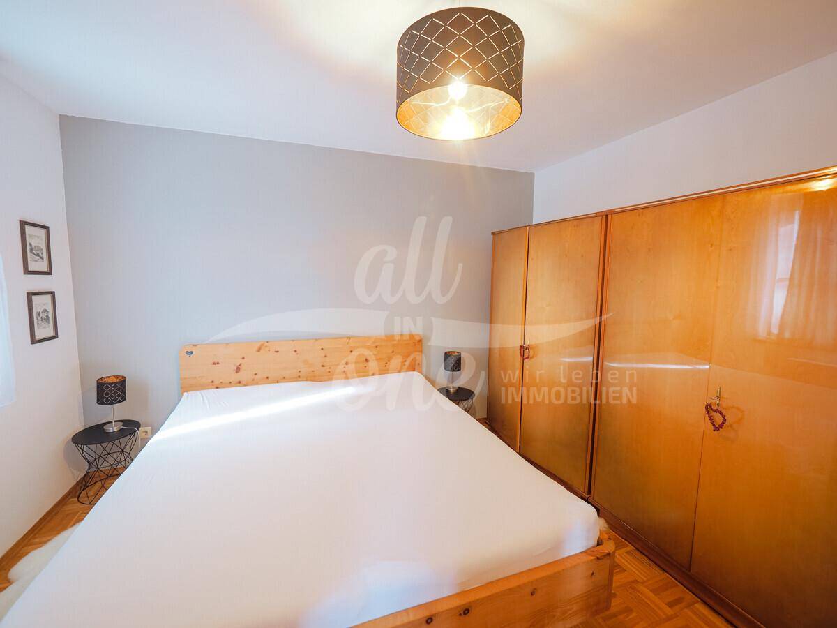 Schlafzimmer mit Doppelbett, Holzschrank und modernem Deckenlicht.